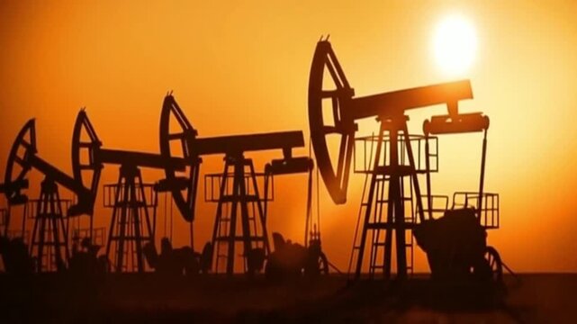 Silhouettes of multiple oil pumpjacks working against a vibrant orange sunset sky, symbolizing energy production and industrial activity.