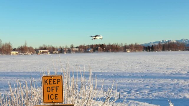 Seaplane taking off from a frozen lake surrounded by snow and mountains in Anchorage, Alaska. 