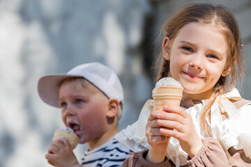 A cute little girl and a boy are eating ice cream on a hot summer day. The children are enjoying a sweet dessert during their summer vacation.