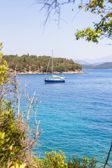 Sailboat on clear blue sea near a rocky coastline and hills
