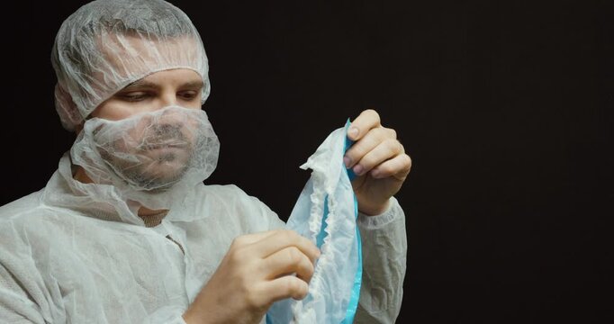 A technician in full protective clothing holds up and presents a blue disposable shoe cover, highlighting hygiene and contamination-control procedures. Ideal for cleanroom manufacturing, medical facil