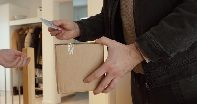Close-up of a courier holding a parcel while verifying the recipient&rsquo;s ID card before completing the handover. Ideal for secure delivery, age verification, proof of identity, fraud prevention, and las