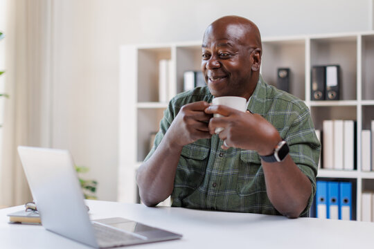Elderly 60s man on laptop holding a coffee cup, senior looking at laptop screen surfing the net, older generation and modern tech application easy usage concept
