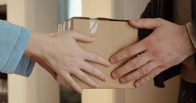 Tight shot of two people&rsquo;s hands handing over a cardboard parcel, capturing the moment of delivery and receipt. Ideal for logistics, e-commerce, shipping, customer service, and last-mile delivery conc