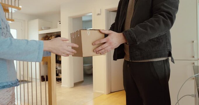 Indoor shot of a delivery person passing a small cardboard package to a woman at home, capturing the moment of receipt. Ideal for e-commerce, home delivery, customer service, logistics, and last-mile