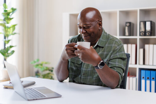 Elderly 60s man on laptop holding a coffee cup, senior looking at laptop screen surfing the net, older generation and modern tech application easy usage concept
