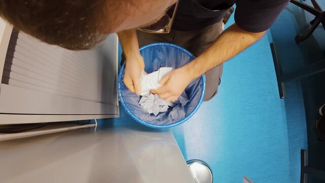 Overhead shot of a stressed person urgently digging through an office trash bin to find a missing sheet with critical information. Strong for concepts like data loss, document disposal mistakes, priva