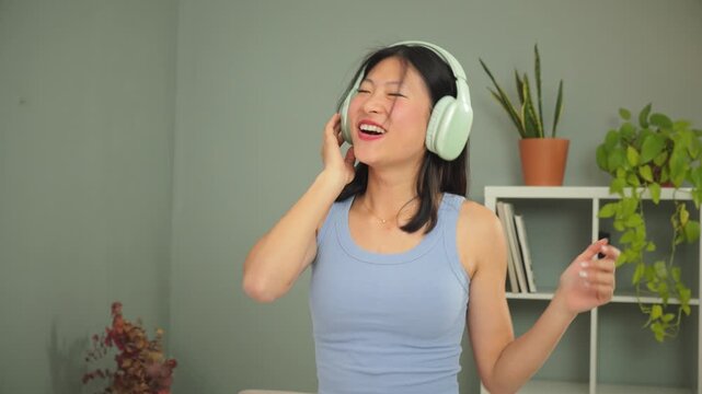 This vibrant young woman enjoys dancing joyfully in her cozy living room, wearing trendy headphones while listening to her favorite music and radiating happiness and energy in a stylish home