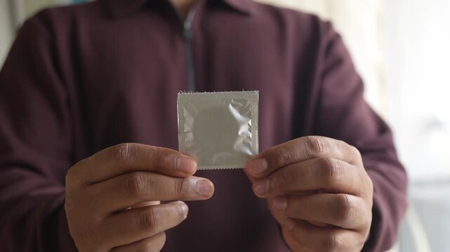 Showing packets of condoms held on finger.