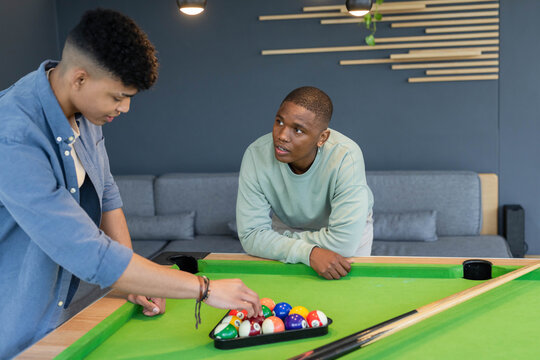 Diverse male friends racking billiard balls into triangle rack on green pool table in lounge