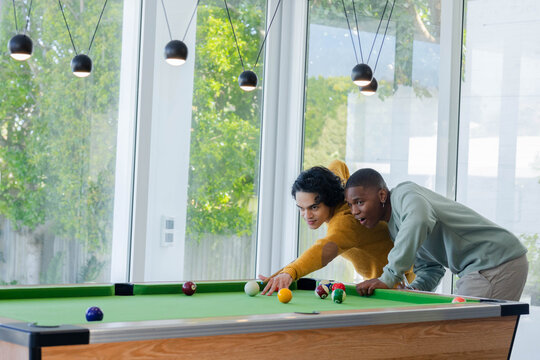 Asian and African American men lining up cue shot while one leaning, guiding at pool table