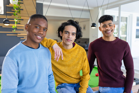 Diverse adult men wearing knit sweaters and jeans posing at pool table with billiard balls