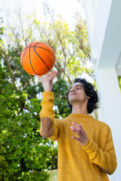 Man spinning orange basketball on finger on porch, wearing mustard sweater with brown elbow patches
