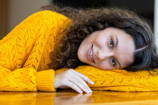 Woman lying on polished wooden floor at home wearing bright yellow knitted sweater, resting