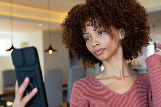African American woman holding smartphone in dining area, wearing ribbed pink top and hoop earring