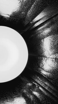 surreal monochrome light orb shining through dimpled foil tunnel with reflective textures and dramatic depth