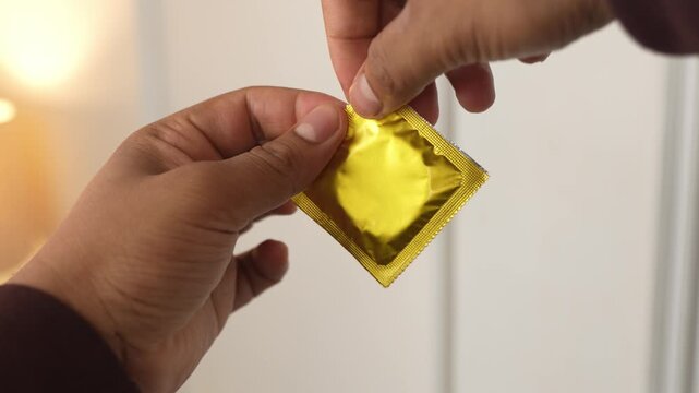 Tearing pack of condom with fingers and showing condom.