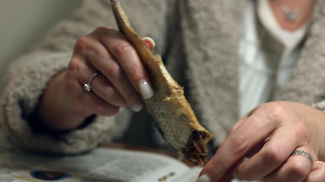 A woman's hands cut up dried raba for eating. A woman cleans dried fish.