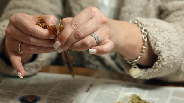 A woman's hands cut up dried raba for eating. A woman cleans dried fish.