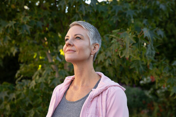 Woman wearing small stud earrings, athletic clothing, gazing upward while standing in backyard