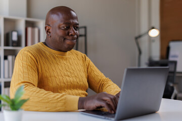 Confident Black senior man using a laptop at home, deep in thought and planning
