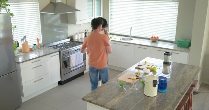 Asian man reaching for woman's hand, playful dancing with African American woman in kitchen avocado