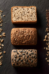 Three Types of Whole Grain Bread with Seeds on Dark Stone Background, Top View