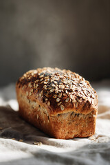 Freshly baked golden multigrain bread loaf topped with oats and seeds on linen cloth, warm steam rising