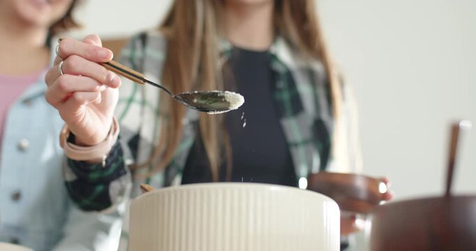Wooden bowl is tilting as teaspoon is tapping and sifting powder into ribbed bowl for baking