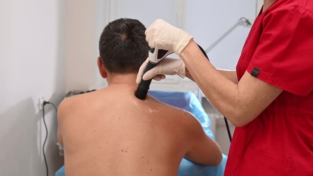 Physiotherapy session with shockwave therapy device on male patient&rsquo;s upper back. Professional therapist treats muscle injury, chronic pain, and posture correction using modern rehabilitation equipmen