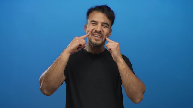 Young hispanic man wearing black shirt gestures expressively against isolated blue background conveying emotion and personality.