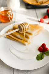 Thin crepes with honey and raspberries on white plate.Stack of thin crepes served with honey, fresh raspberries, and mint on a white plate. Bright natural light, clean background, and shallow depth of