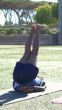 Vertical video: Cueing child in blue shirt and shorts barefoot doing core leg stretches on turf mat