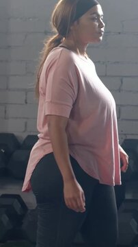 Vertical video: Walking lady in pink tee, pants passing weights at gym hearing call checking watch