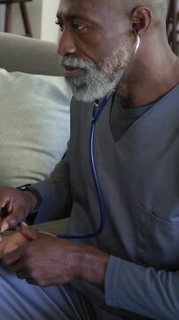 Vertical video: Checking pulse doc in scrubs with stethoscope after patient offering arm on sofa