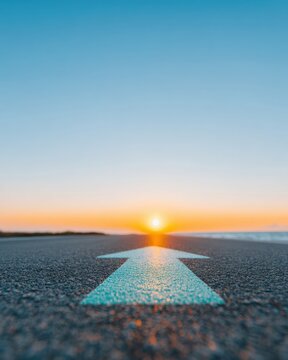 Asphalt highway with painted arrow pointing toward sunset symbolizing new beginnings and career path opportunities for motivational business background with copy space