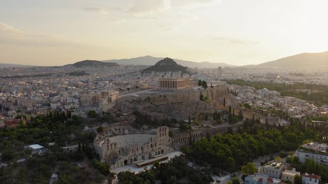 Slow pan drone shot of the Acropolis and Parthenon at sunrise, revealing the Odeon of Herodes Atticus and Lycabettus Hill under soft golden light