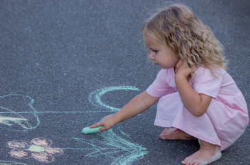 Naklejka premium Cute little girl drawing a colorful rainbow with chalk on the asphalt road
