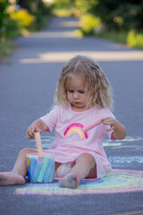 Fototapeta premium Cute little girl drawing a colorful rainbow with chalk on the asphalt road