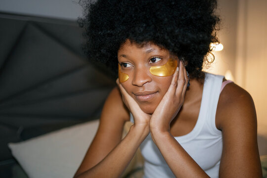 Thoughtful woman with eye patches sitting on bed in evening