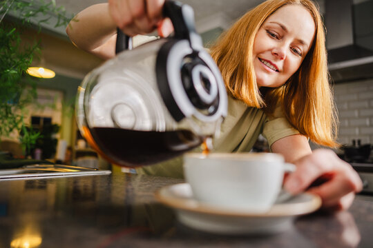 Smiling woman pours coffee into cup during morning routine at home