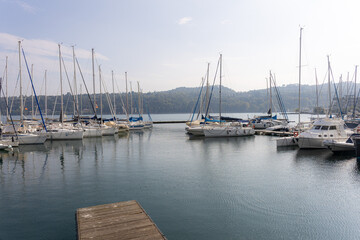 Obraz premium Marina with moored sailboats and masts on calm water. Wooden dock in foreground, hills in background. Wide horizontal composition with copy space