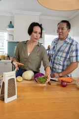 Selbstklebende Fototapeten Zu Kochen Diverse couple preparing vegetables with knife and cutting board at kitchen island with bowl  © wavebreak3