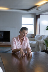 Naklejka premium Senior woman sitting at wooden dining table wearing shirt in living room with projector