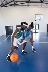 Obraz premium African american males dribbling and guarding basketball on court in gym near hoop by door