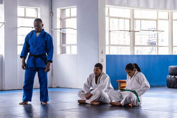 African american instructor standing at dojo with students adjusting belts near tires, copy space