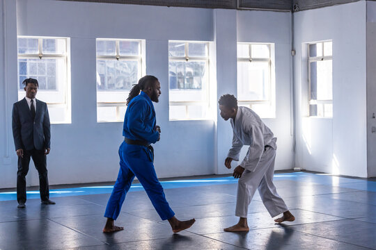 African american coach and students engaging in sparring on mats wearing gis near windows