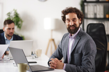 Business team works together in office. One person smiles at the camera while others focus on discussions and tasks. Meeting encourages idea sharing and collaboration among team members.