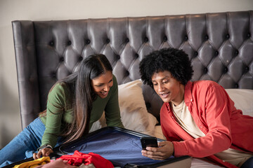 African american and indian couple sorting clothes, checking smartphone on suitcase in bedroom © wavebreak3