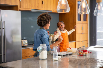 African american mother with daughter whisking batter on kitchen island with mixing bowl and whisks
